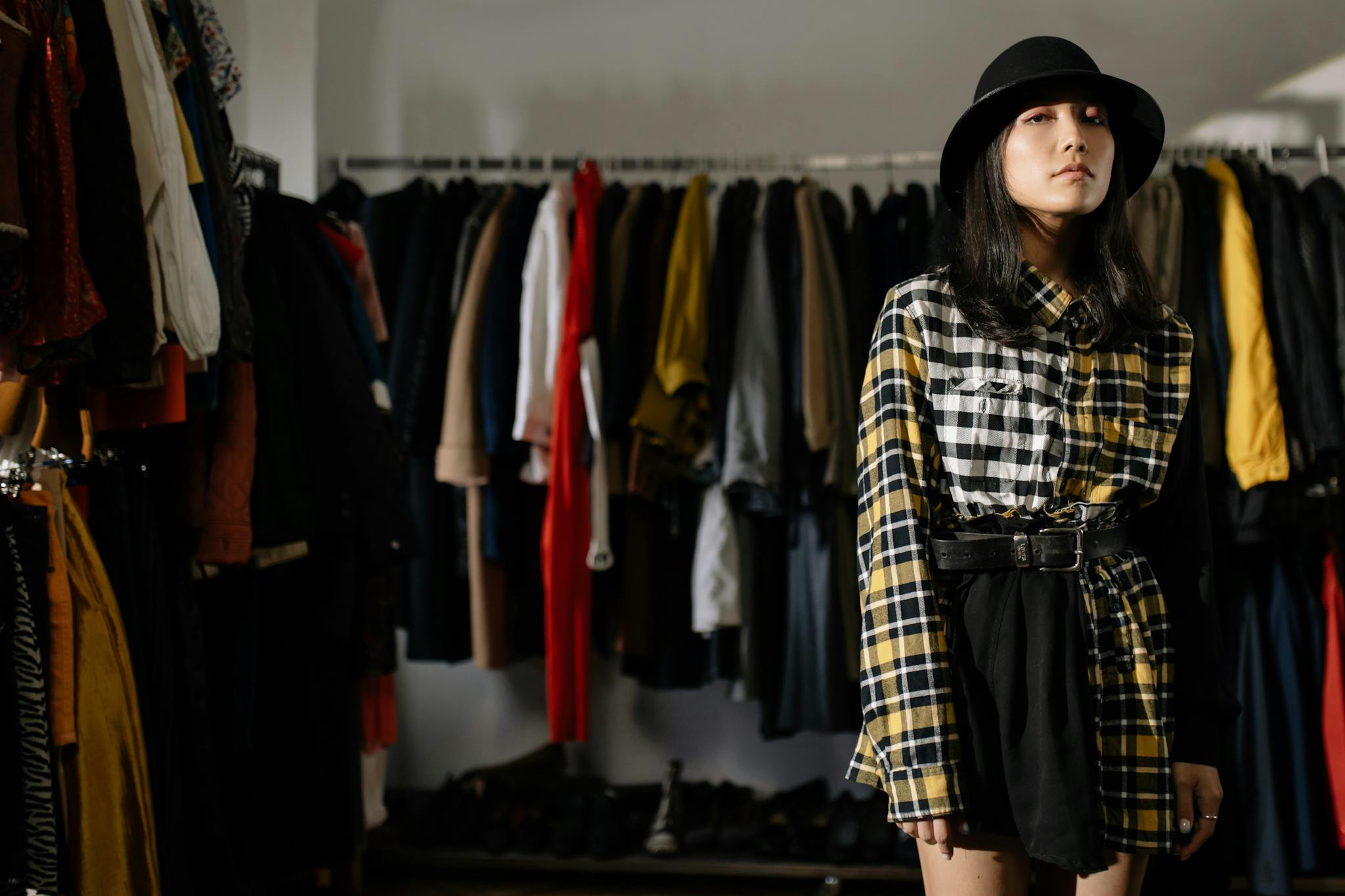 Stylish woman poses in a chic plaid outfit at a thrift store, embracing sustainable fashion.