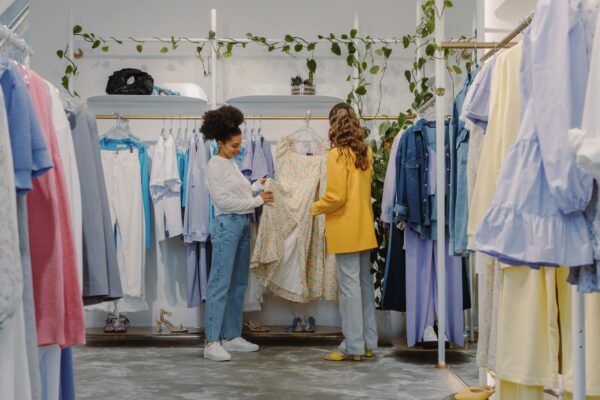Two women shopping for trendy outfits in a modern clothing boutique filled with colorful garments.